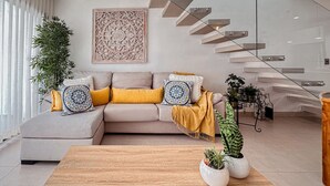 Een moderne woonkamer met een bank, decoratieve kussens, een houten salontafel en een potplant.