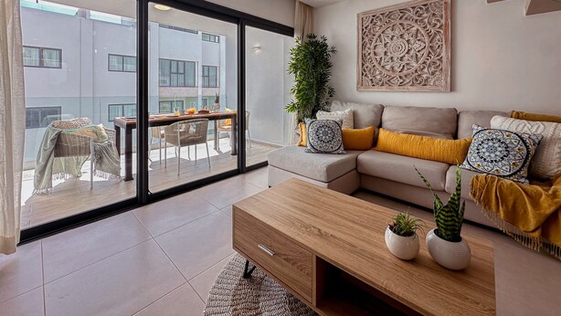 Een moderne woonkamer met een bank, salontafel en uitzicht op een balkon met tuinmeubilair.