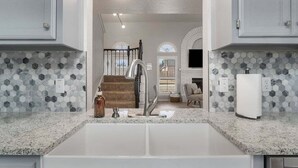 A kitchen with a granite countertop, a double sink, and a backsplash with hexagonal tiles. - South Tulsa Splash W/Pool & Hot Tub (Tulsa)
