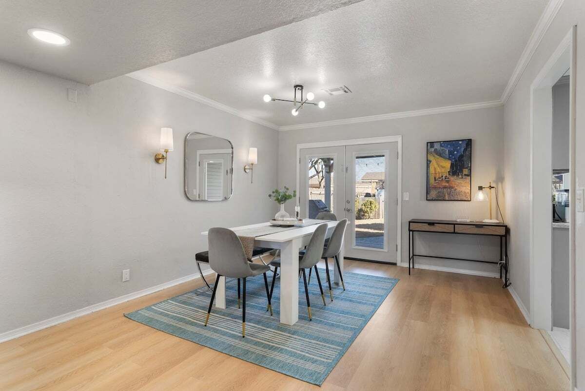 A dining area with a white table, grey chairs, a blue rug, and a ceiling light fixture.