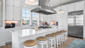 A modern kitchen with white cabinetry, stainless steel appliances, and a central island with bar stools. - Pet-Friendly, Pool-Side 6BR Beach Home in Cinnamon Shore With 20+ Amenities (Port Aransas)