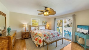 A bedroom with a bed, a ceiling fan, a television, a window with a view of the outdoors, and a wooden dresser. - Sassy Seahorse: Heated pool, hot tub, ping pong, Foosball and pool table! (Anna Maria)