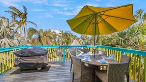 An outdoor deck with a table set for dining, a covered grill, and a yellow umbrella. - Sassy Seahorse: Heated pool, hot tub, ping pong, Foosball and pool table! (Anna Maria)