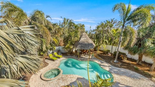 A swimming pool with a thatched roof structure, surrounded by palm trees and lounge chairs. - Sassy Seahorse: Heated pool, hot tub, ping pong, Foosball and pool table! (Anna Maria)