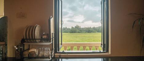 A kitchen with a window view of a green field and a balcony.