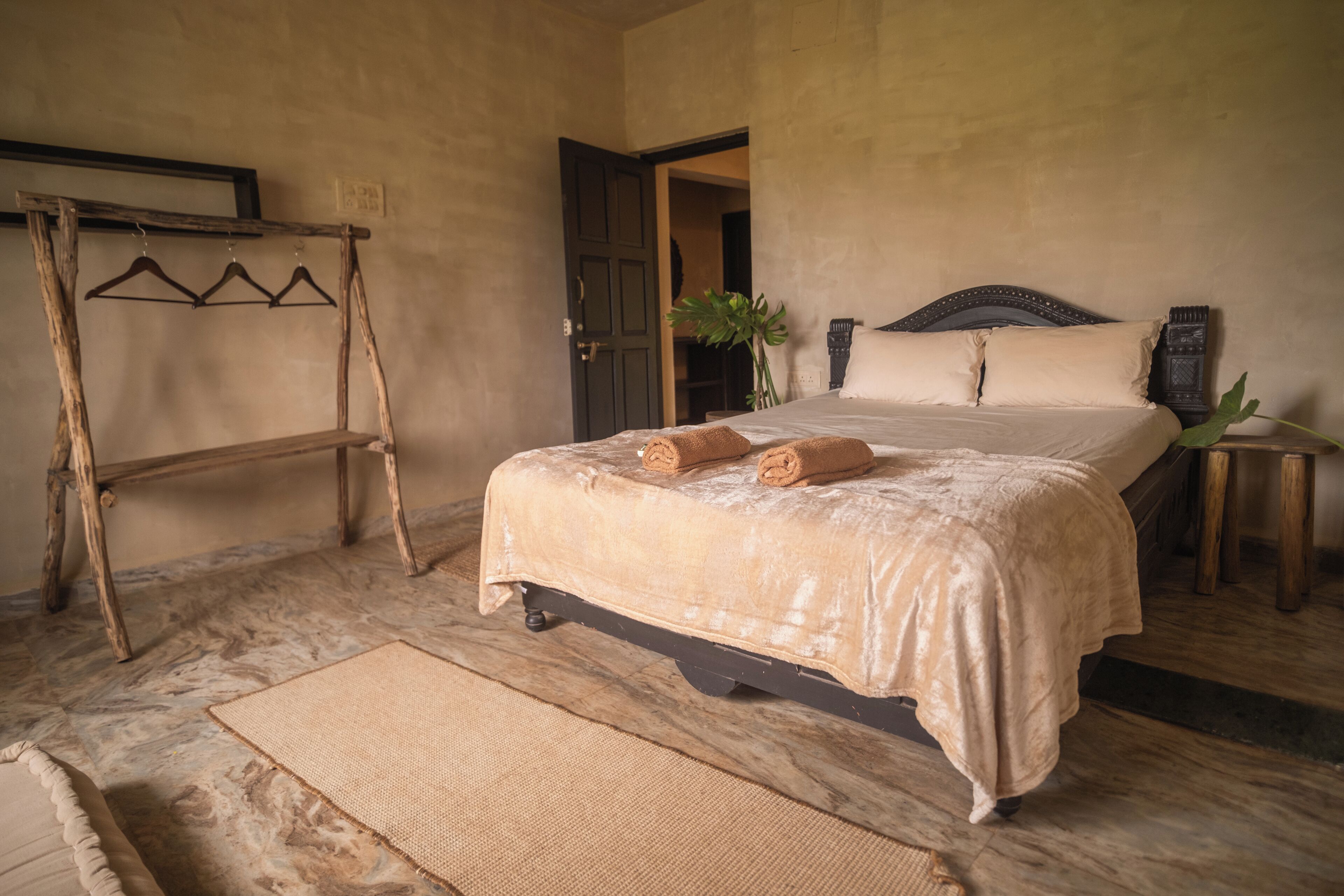 A bedroom with a bed, a wooden hanger rack, a plant, and a small table.
