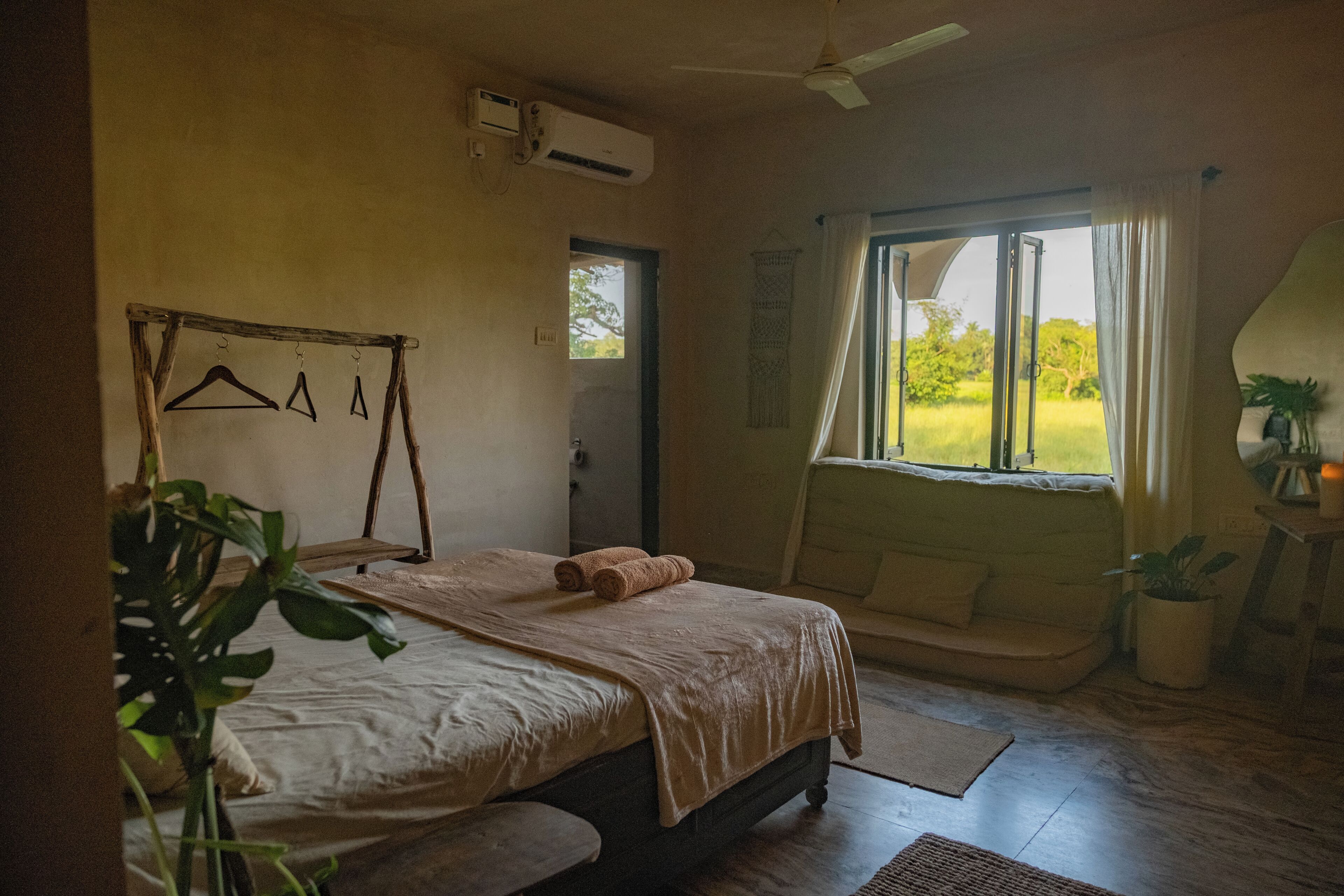 A bedroom with a bed, a hanging clothes rack, a window with curtains, and a ceiling fan.