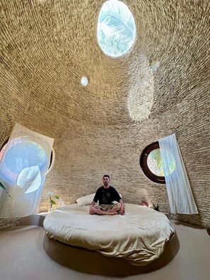A room with a circular bed, a small window, and a textured ceiling.