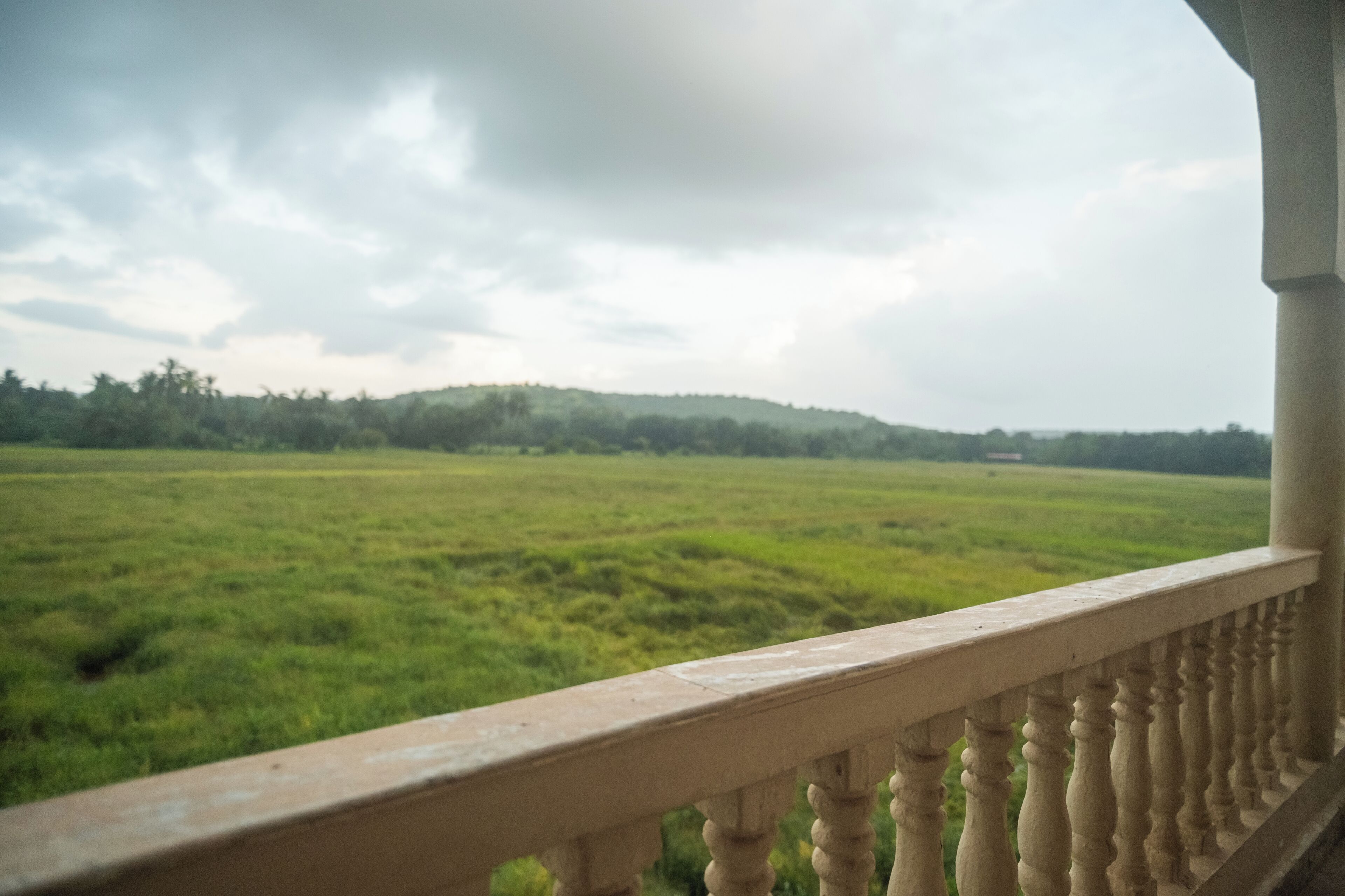 A balcony with a view of a green field and a cloudy sky.