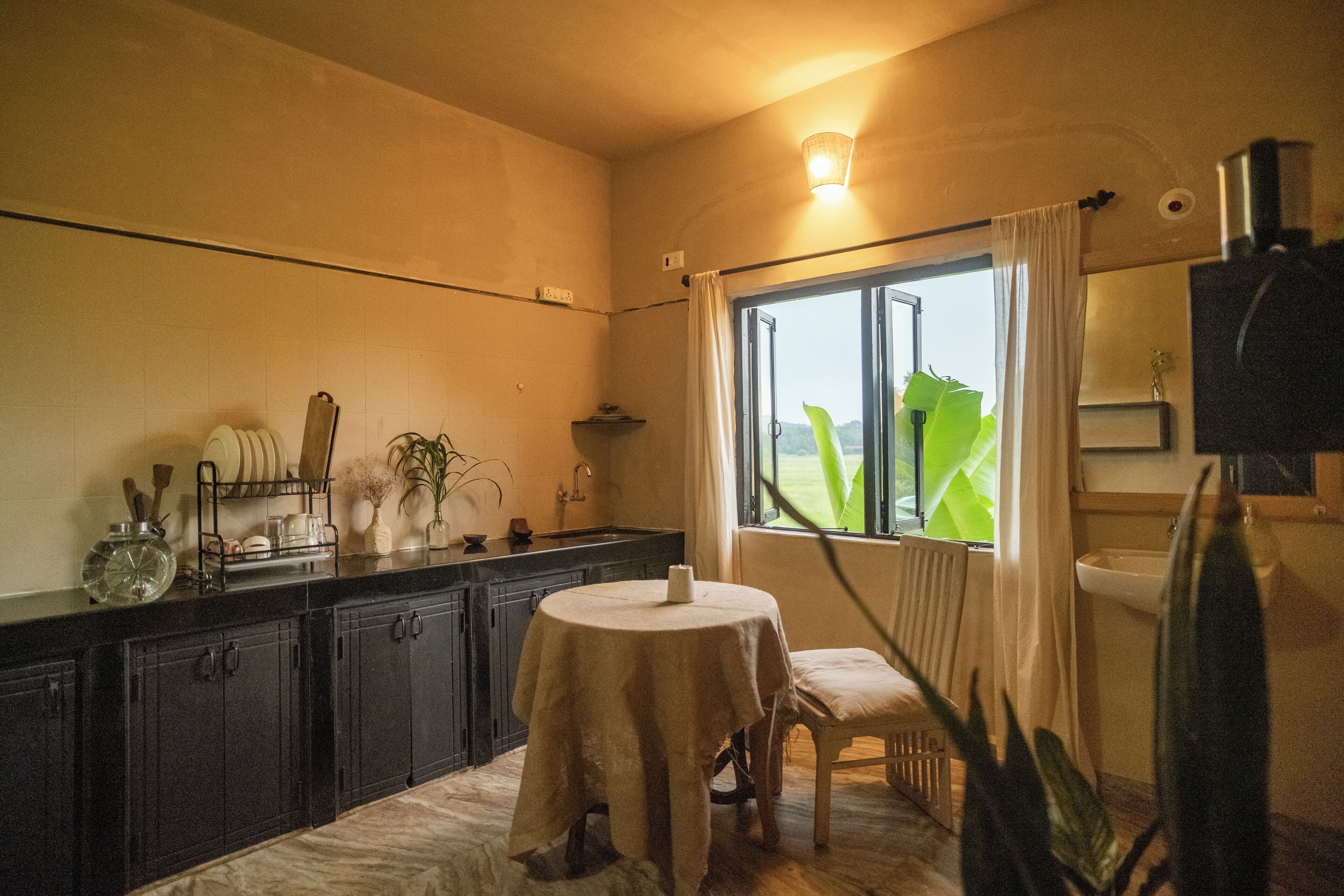 A kitchen with a round table, cabinets, and a window with curtains.