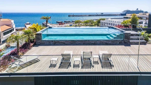 A rooftop infinity pool with lounge chairs, a view of the sea, and a cruise ship in the background. - Luxury Rooftop Jacuzzi Penthouse at Savoy Insular (Funchal)