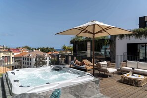 Une terrasse sur le toit équipée d’un jacuzzi, de chaises longues et d’un parasol.
