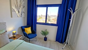 A bedroom with a bed, a chair, a bedside table with a lamp, a window with curtains, and a plant. - Vacation apartment Costa Sun, Costa Calma, pool, WiFi, balcony (Costa Calma)