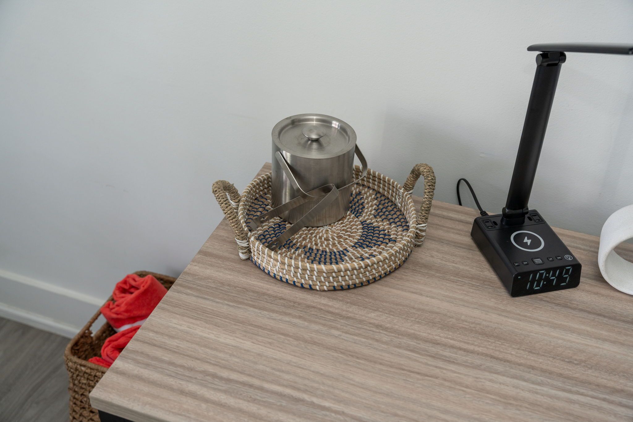 Ein gewebter Korb mit einem Edelstahlkochtopf auf einem Holztisch, einem schwarzen mobilen Ladegerät und einem roten Handtuch in einem Korb.