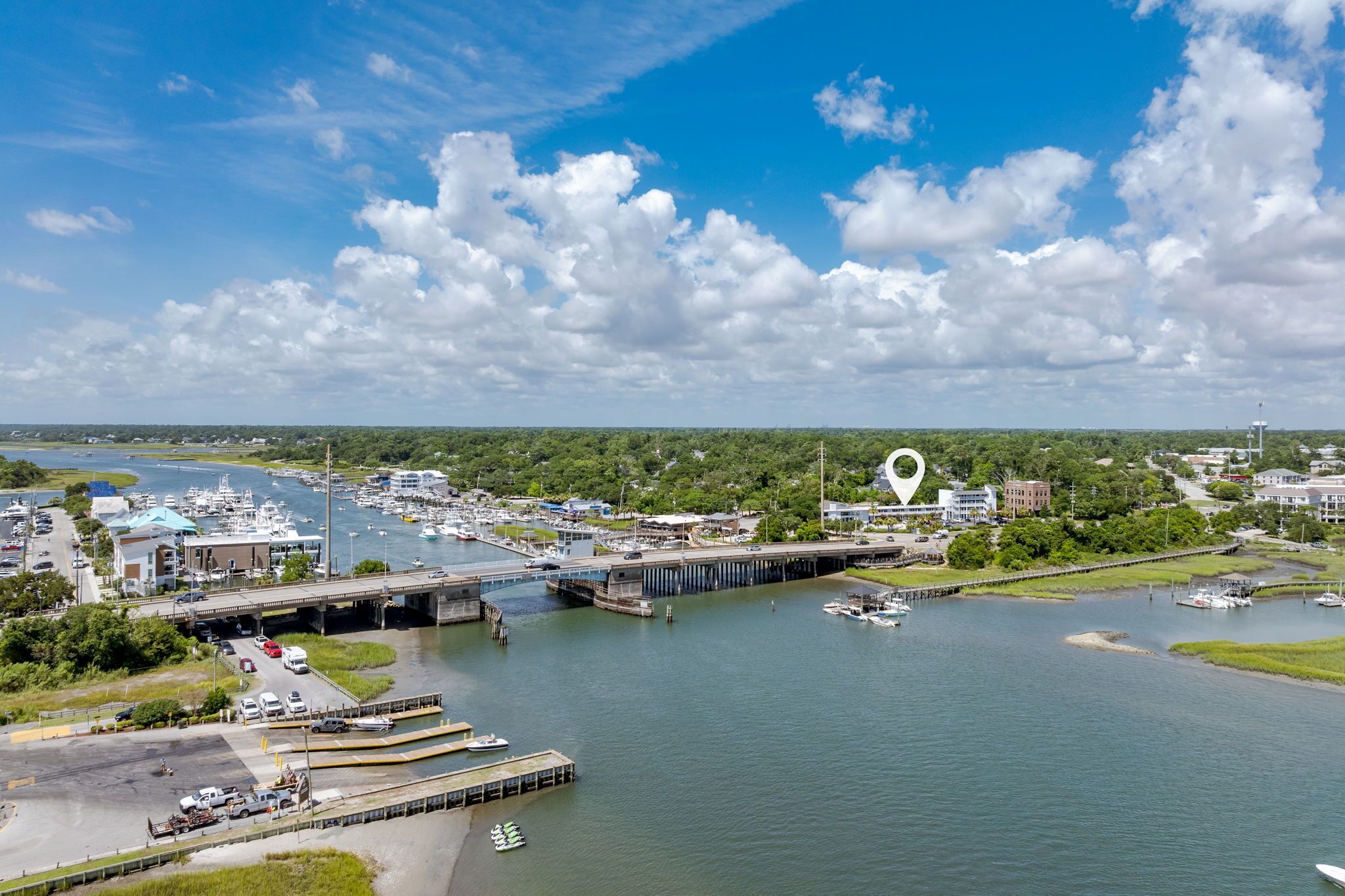 An aerial view of a marina with boats, a bridge, and surrounding greenery.