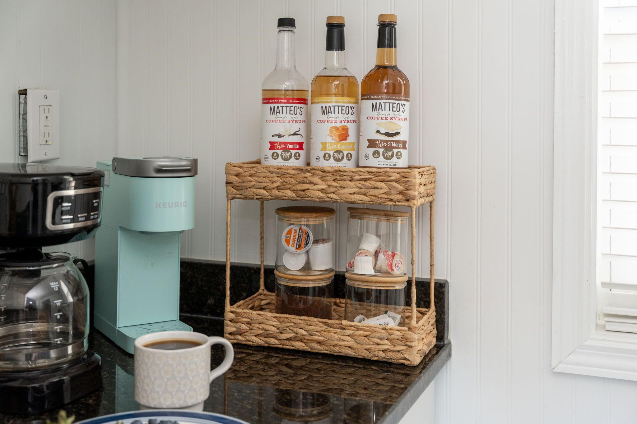 Una cocina con una cafetera Keurig, un dispensador de café y tres botellas de sirope para café Mattéo's.