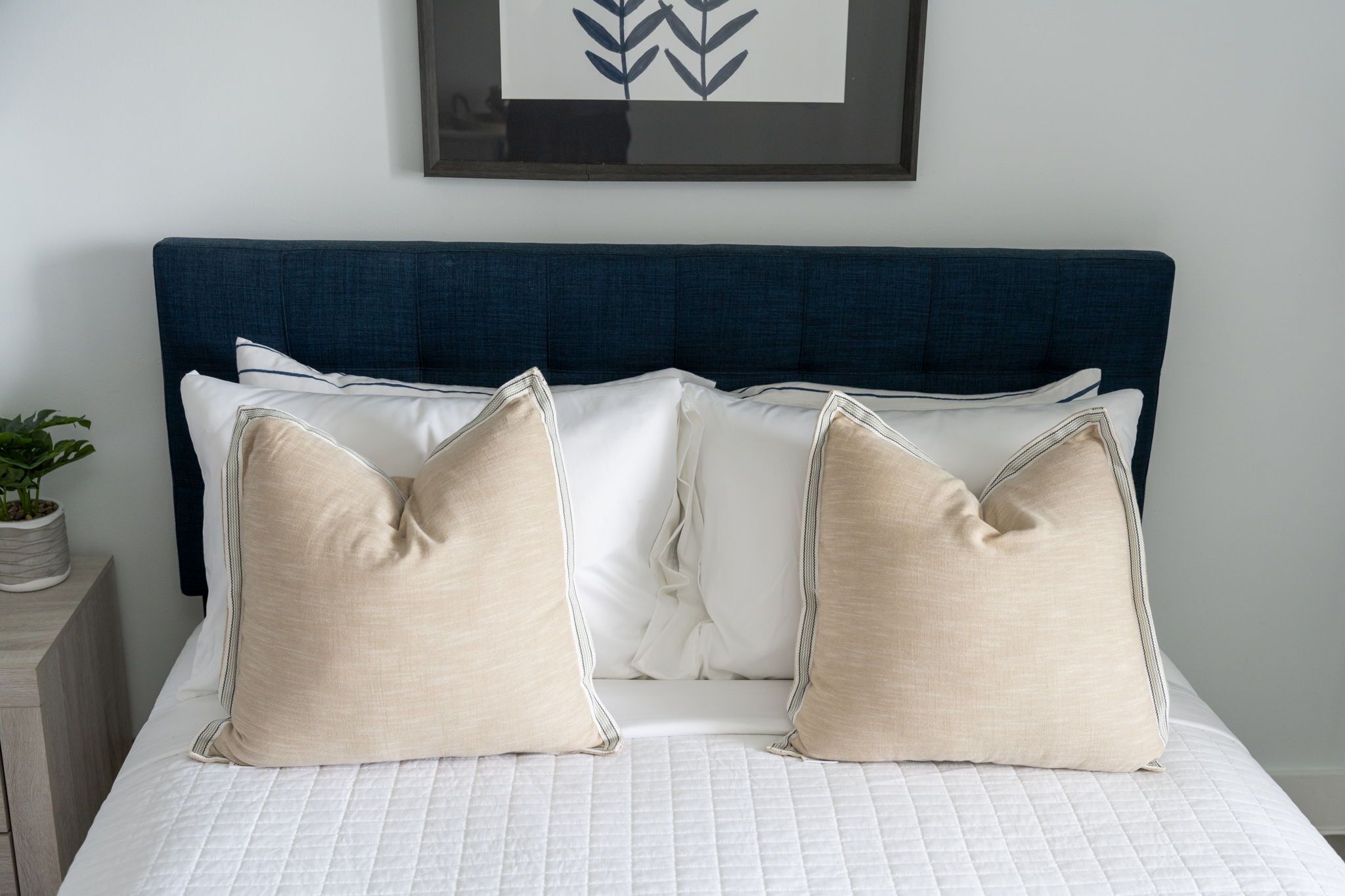 Una cama con cabecera azul oscuro, ropa de cama blanca y almohadas color beige.