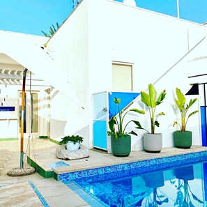 A poolside area with a white building, a blue door, and potted plants. - Casa Mondrian - Camere con Bagno e Piscina Privata (Tiggiano)
