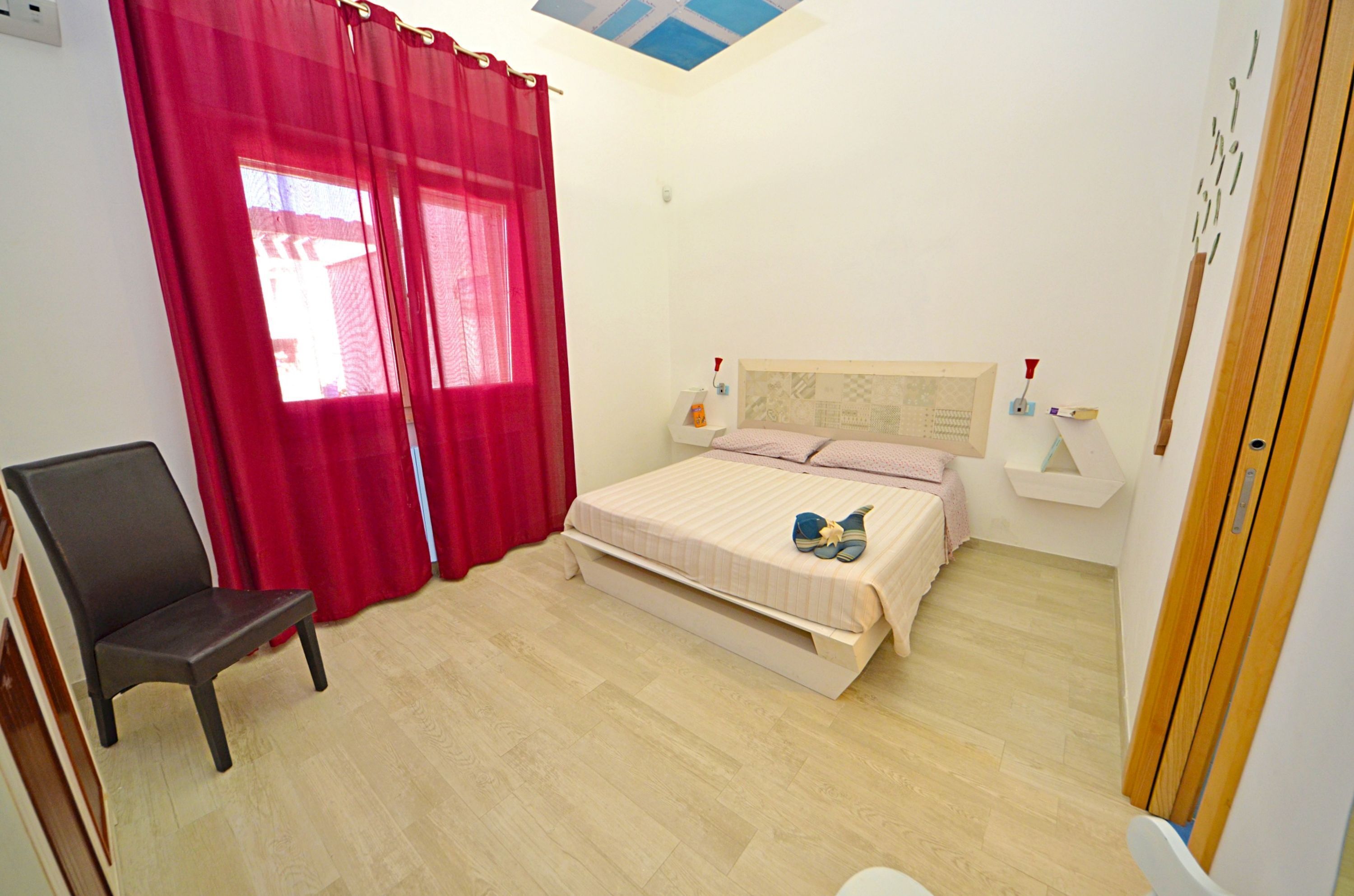 Un dormitorio con cama, una silla y una ventana con cortinas rojas.