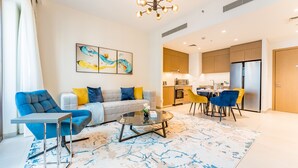 Una sala moderna con sofá, mesa de centro y sillas, un área de cocina con armarios y refrigerador, y una mesa de comedor con sillas.