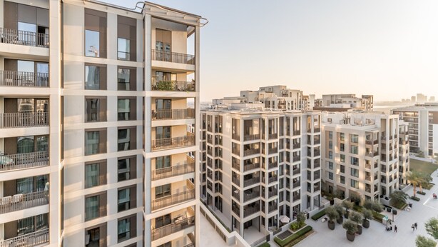 Un edificio residencial alto con varios balcones, un jardín en la azotea y un patio espacioso.