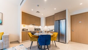 Una cocina moderna con armarios de madera, un refrigerador de acero inoxidable y un comedor con dos sillas amarillas y un mantel azul.
