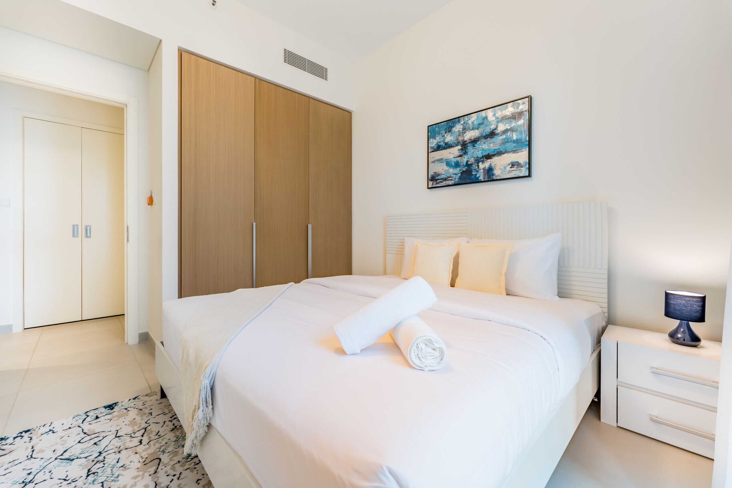 Une chambre à coucher bien rangée, avec un grand lit, une armoire en bois et un tableau accroché au mur.