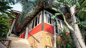 A staircase leading to a red and white building with stone walls, surrounded by tropical vegetation. - Casamata (Búzios)