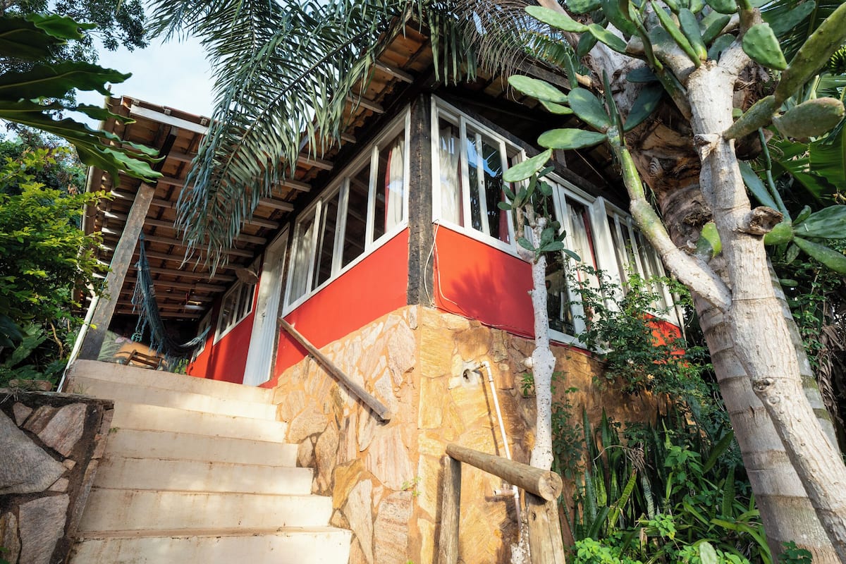 A staircase leading to a red and white building with stone walls, surrounded by tropical vegetation.
