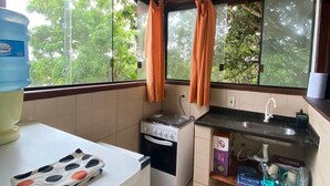 A compact kitchen with a gas stove, a sink, and a window with curtains. - Casamata (Búzios)