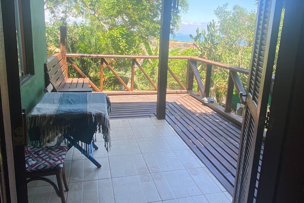 A covered outdoor area with a table and chairs, a wooden deck, and a view of greenery and a body of water.