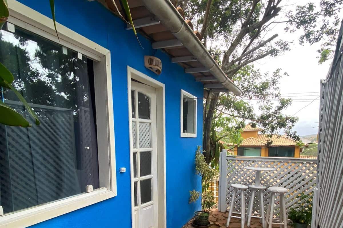 A blue house with a white door, a small patio with stone flooring, and a white fence with a lattice design.