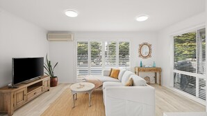 A modern living room with a flat-screen TV, a sofa, a coffee table, and a potted plant. - Cerulean Getaway in Cowes (Cowes)
