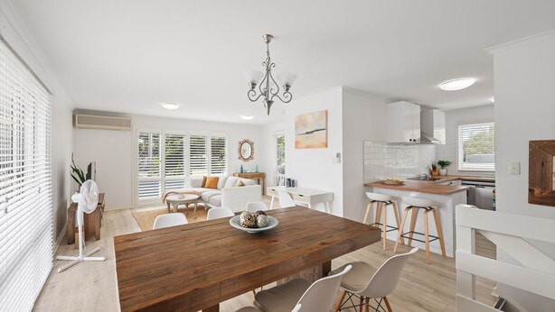 A modern kitchen with a wooden dining table, white chairs, and a central island with stools. - Cerulean Getaway in Cowes (Cowes)