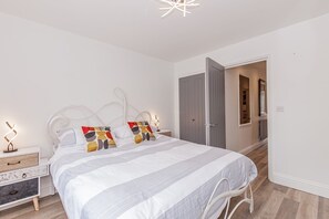 Een slaapkamer met een bed, nachtkastjes, een kledingkast en een deur naar een andere kamer.