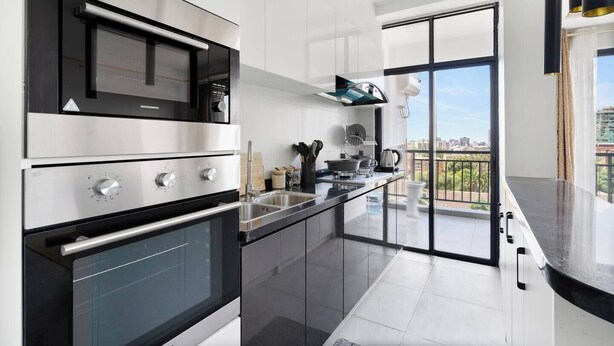 Een moderne keuken met roestvrijstalen apparatuur, een zwart aanrecht en een groot raam met uitzicht op een stadsbeeld.