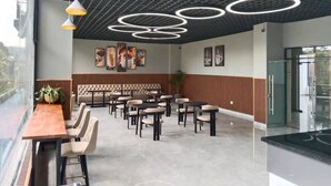 Een moderne eetruimte met een lange houten tafel en meerdere stoelen, een hoog plafond met ronde lampen en uitzicht door grote ramen.