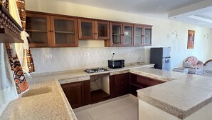A modern kitchen with granite countertops, wooden cabinets, and a built-in microwave. - Mulla Apartments  (Malindi)