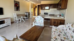 A spacious living room with a sofa, a coffee table, and a dining area with chairs and a table. - Mulla Apartments  (Malindi)