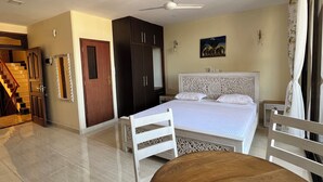 A bedroom with a bed, a ceiling fan, a nightstand, a chair, and a wooden table. - Mulla Apartments  (Malindi)