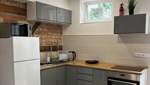 A compact kitchen with grey cabinets, a white refrigerator, a microwave, a kettle, and a built-in oven. - Apartments Badallee 4, Bad Schandau, apartment no. 8, 50m2 (Bad Schandau)
