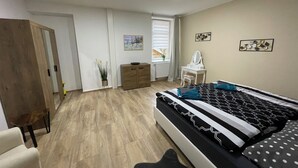 A bedroom with a bed, a dresser, a vanity, and a window with blinds. - Apartments Badallee 4, Bad Schandau, apartment no. 8, 50m2 (Bad Schandau)