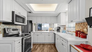 Una cocina moderna con armarios blancos, electrodomésticos de acero inoxidable, suelo de madera y tragaluz.