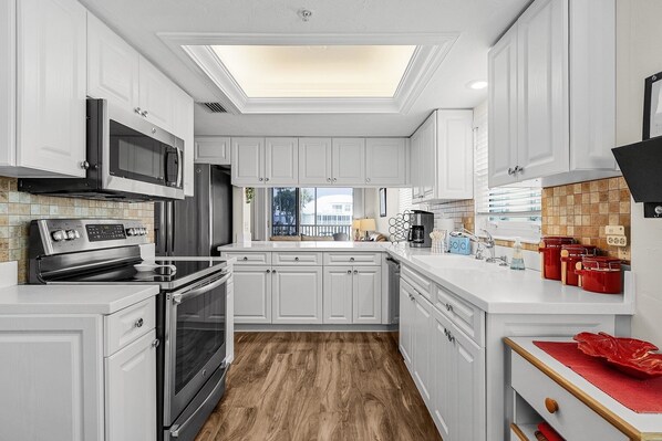 Una cocina moderna con armarios blancos, electrodomésticos de acero inoxidable, suelo de madera y tragaluz.