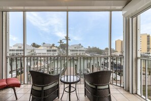 A balcony with wicker chairs and a small table, overlooking a marina with boats and buildings. - Casa Marina 144 2 Bedroom Condo (Fort Myers Beach)