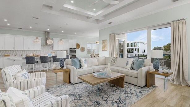A spacious living area with a sofa, armchairs, and a coffee table. There is a kitchen in the background with white cabinets and a dining area with chairs. - Brand New Luxury Build 265 Carolina Ave: Heated Pool, Hot Tub 6 Bedroom Home (Fort Myers Beach)