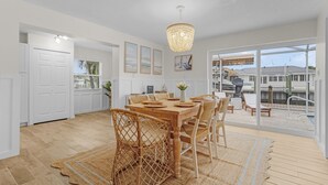 Une salle à manger spacieuse, avec une table et des chaises en bois, un lustre et de grandes fenêtres donnant sur l’extérieur.