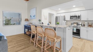 Une cuisine moderne avec des meubles blancs, un îlot central doté de tabourets, un four à micro-ondes, un réfrigérateur et un four.