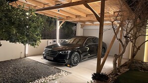 Ein schwarzes Auto steht unter einer Holnpergola in einem überdachten Außenbereich mit Kiesweg und kleinem Garten.