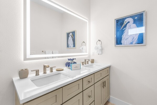 A modern bathroom with a large mirror, two sinks, and a vanity with cabinets.